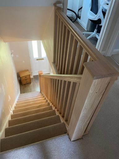 Wooden staircase leading downwards with a railing and light coming from a window.