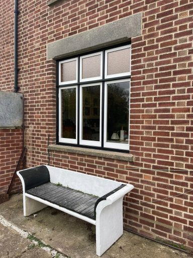 A white bench beside a brick wall with a large window above it.