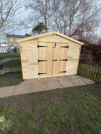 Wooden shed with double doors, set on a path in a grassy area.